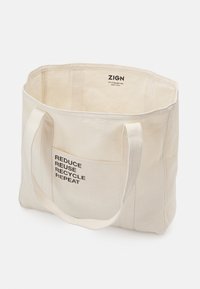 Sac fourre-tout en coton beige avec longues anses et poche avant imprimée du texte "RÉDUIRE RÉUTILISER RECYCLER RÉPÉTER" en noir.