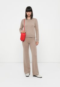 Beige strikkegenser og vidt bukse sett, kombinert med en liten rød håndveske. Outfiten har en myk tekstur og en avslappet passform.