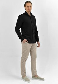 Zwarte langarm overhemd met een puntige kraag, gecombineerd met beige broek en lichtgrijze instapschoenen. Eenvoudige, op maat gemaakte pasvorm.