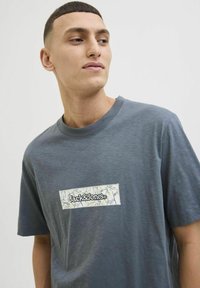 Grå t-shirt med korte ærmer, der har et rektangulært blomstermotiv med "Jack & Jones" tekst, glat stof og rund halsudskæring.