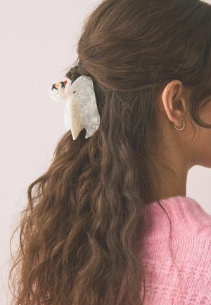 Long brown wavy hair half-up secured with a white swan-shaped hair clip, worn by a person with a gold hoop earring and pink knit sweater.