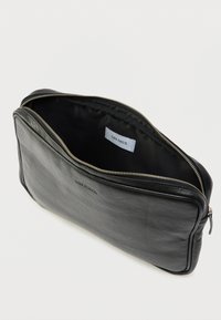 Czarna skórzana saszetka o fakturowanej powierzchni, z zamkiem błyskawicznym i podszewką z tkaniny wewnątrz. Posiada subtelne logo i kontrastujące przeszycia.