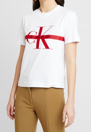 Bílé bavlněné tričko s výrazným červeným logem "CK" a vodorovným červeným pruhem s textem "CALVIN KLEIN JEANS" v tučném písmu.
