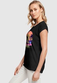 Svart t-skjorte med korte ermer som har et fargerikt solnedgangsdesign med palmer, rosa og lilla nyanser, samt en avslappet passform.