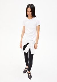 Hvid ribbet t-shirt med en bundet hvid skjorte i taljen, parret med sorte leggings og spidse sorte sko med ankelstropper.