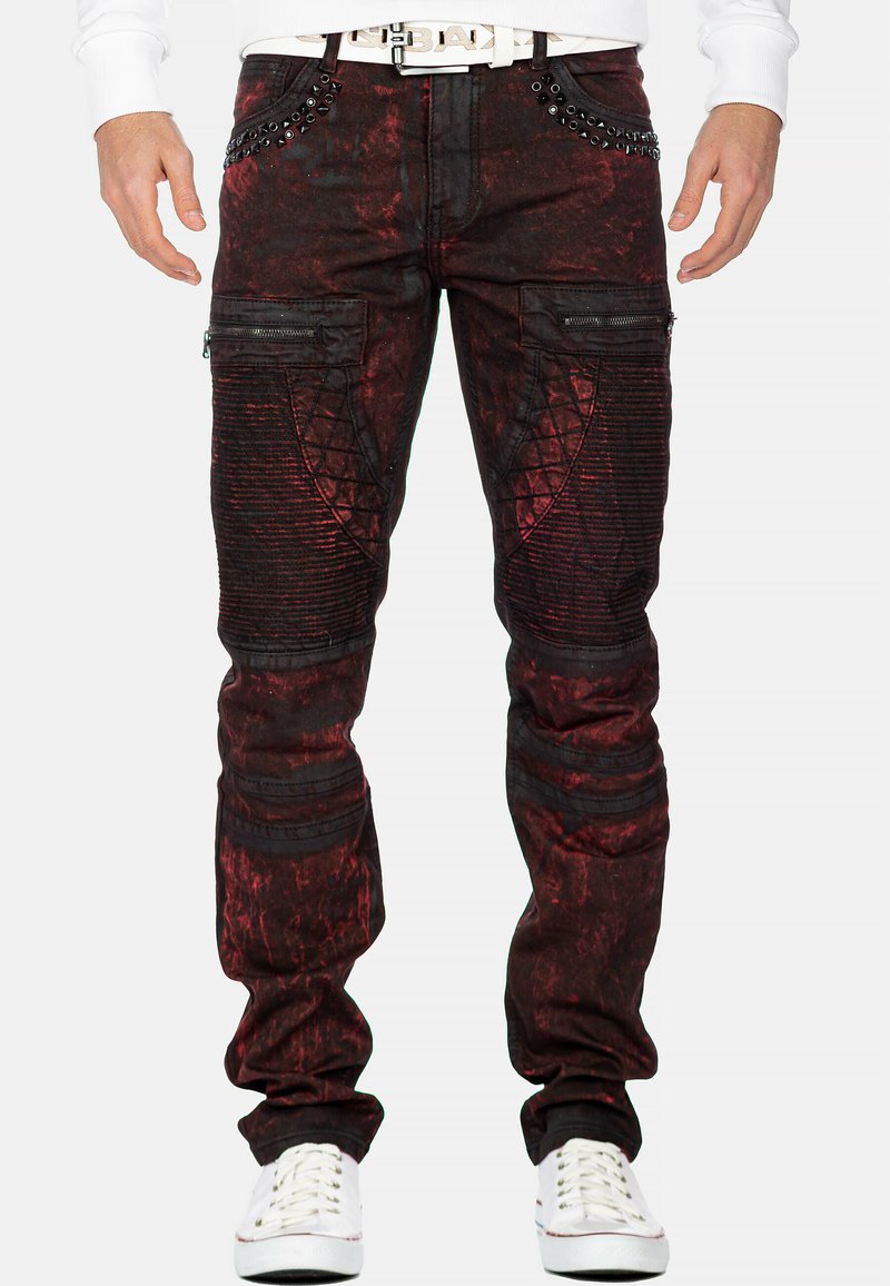 Pantaloni da uomo rossi e neri con effetto usurato, tasche con zip, dettagli testurizzati e borchie sulla vita. Materiale in misto cotone.