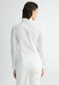 Weißes Langarmhemd mit elegantem Design, aus glattem Stoff gefertigt. Mit einem Kragen, Knopfdetails am Hals und an den Manschetten sowie geradem Schnitt.