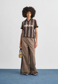 Black and brown striped short-sleeve polo with pink branding, paired with wide-leg leopard print pants and holding a small bag.