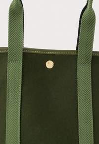 Zelená taška přes rameno z plsti se strukturovanými zelenými popruhy, zlatým kováním a kontrastním šitím podél horního okraje.