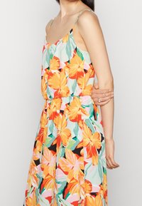 Bloemige maxi-jurk met een losse pasvorm, met levendige oranje en teal bloemen op een lichte achtergrond, en dunne verstelbare spaghetti-bandjes.