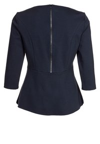 Marinblå peplumtop med trekvartslånga ärmar, konturerade sömmar och dragkedjestängning bak. Tillverkad av ett slätt, strukturerat tyg.