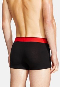 Shorts en coton noirs avec une large ceinture rouge et une fine bordure noire, présentant une texture lisse et un design ajusté.