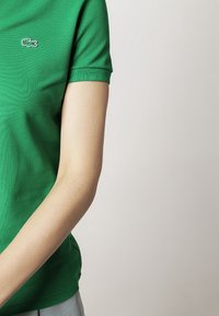 Polo vert en tissu texturé, avec un petit logo brodé sur le côté gauche de la poitrine et un col classique côtelé.