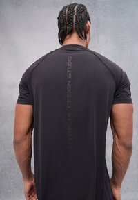Camiseta atlética negra de manga corta, con una textura suave y un logo impreso en una tonalidad más clara en la parte posterior.