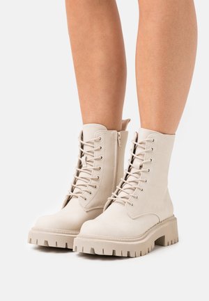 Bottines à lacets en suède beige, avec une semelle épaisse à crans, une fermeture éclair latérale et un col légèrement rembourré.