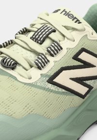 Lichtgroene sportschoen met gestructureerde stof, donkergrijze accenten en gestreepte veters. Voorzien van een opvallend "N"-logo in contrasterende kleuren.