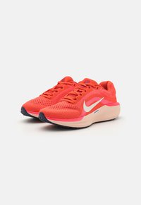 Helle orange Laufschuhe mit Obermaterial aus Mesh, lila Akzenten, gepolsterter Sohle und weißem Swoosh-Logo. Verfügt über Schnürsenkel und ein strukturiertes Muster.