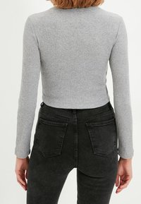 Grå ribbad långärmad topp med en kortad skärning, i kombination med högmidjade svarta denimjeans med bakfickor och en strukturerad yta.