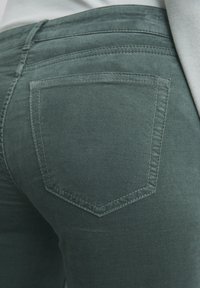Groene stretch spijkerbroek van denim met een vijf-pocket ontwerp. De achterkant heeft een enkele gestikte, diamantvormige zak. Soepele textuur.