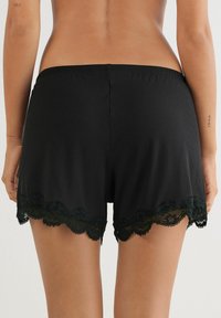 Zwarte geribde stofshorts met een geschulpte kanten zoom in donkergroen. De tailleband is elastisch voor extra comfort.