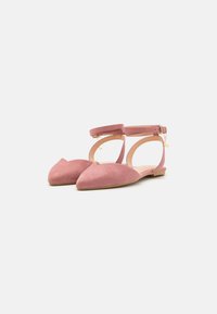 Bailarinas de ante rosa con punta afilada y correas para el tobillo. Presentan una hebilla en tono dorado y un diseño cortado minimalista.