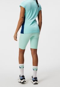 Een lichtblauw sportshirt met korte mouwen, gecombineerd met mintgroene shorts. Witte sokken met een geometrisch patroon, gedragen met meerkleurige schoenen.