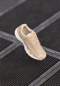 Baskets beiges avec un matériau en maille et synthétique, une surface texturée, un col rembourré et une semelle blanche avec des accents gris.