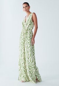 Abito lungo in tessuto leggero con motivo verde e bianco. Presenta una profonda scollatura a V, una cintura regolabile in vita e spacchi laterali per facilitare il movimento.