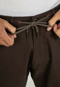 Braune Cordhosen mit einer strukturierten Oberfläche, ausgestattet mit einem Kordelzugverschluss mit Metallenden und Gürtelschlaufen.