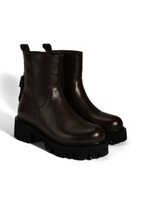 Bottines en cuir marron avec une finition texturée, semelle en caoutchouc noir épaisse, languette et zip latéral pour un accès facile.