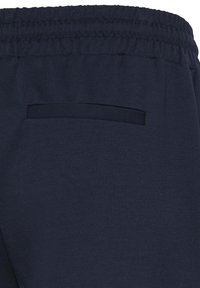 Pantalon à taille élastique bleu foncé avec une poche passepoilée simple à l’arrière, fabriqué en tissu lisse.