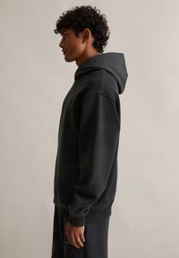 Czarna dresowa bluza z kapturem o luźnym kroju i mankietami. Wykonana z miękkiego materiału, z kieszenią z przodu i minimalistycznym wzornictwem.