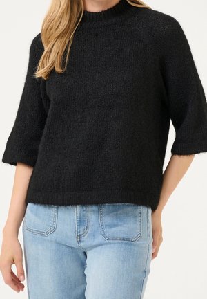 Pull en maille noir avec un col haut et des manches courtes, présentant une finition texturée. Associé à un jean en denim bleu clair.