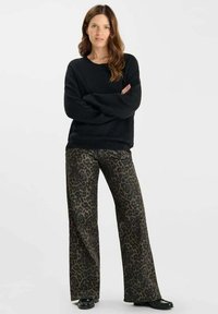 Maglione nero con texture e maniche lunghe abbinato a pantaloni leopardati a gamba larga. Le calzature hanno una finitura lucida.