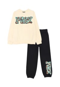 Felpa crema con grafica colorata "PYREX" sul davanti, abbinata a pantaloni della tuta neri con lo stesso logo sulla gamba. Tessuto in misto cotone.