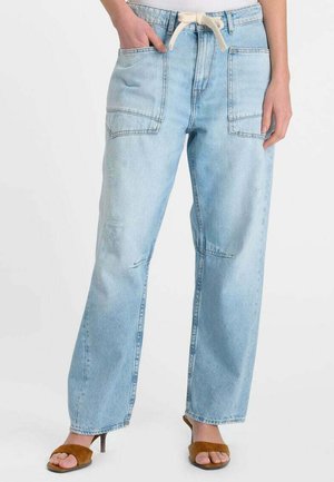 Lichtblauwe denim jeans met hoge taille, voorvakken met klep en een taille met trekkoord, gedragen met bruine sandalen met open teen en hak.