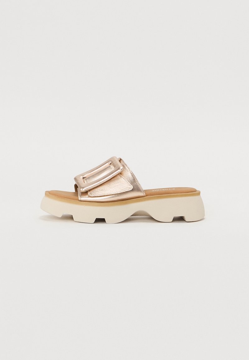 Sandale à glissière unique en or rose avec une grande boucle sur une semelle blanche épaisse texturée sur fond clair.