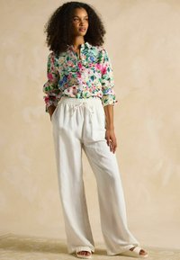 Floral gemustertes Hemd mit lebendigen Farben, lockere weiße Hosen mit elastischem Bund und hellfarbene Slip-On-Schuhe.