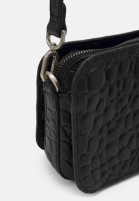 Czarna skórzana torba na ramię z chropowatą, fakturowaną powierzchnią, zamknięciem na zamek i srebrnymi akcentami. Kompaktowy i prostokątny design.
