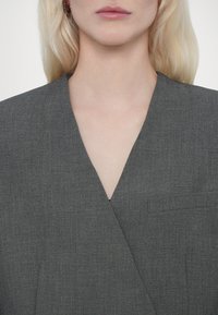 Grijze textuurblazer met een scherpe V-halslijn. Bevat een enkele borstzak en heeft een getailleerd ontwerp, geschikt voor formele settings.