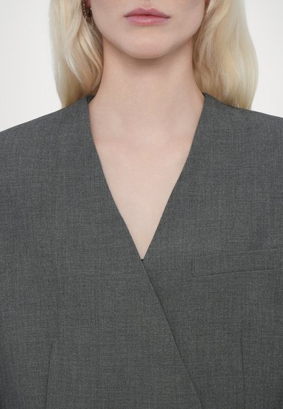 Blazer grigio texturizzato con profondo scollo a V. Presenta una tasca sul petto e un design attillato, adatto a contesti formali.