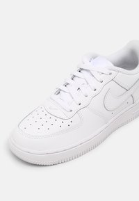 Białe skórzane buty sportowe z perforowanym noskiem, płaskimi sznurówkami, wyściełanym kołnierzem i teksturowaną gumową podeszwą. Zawierają subtelną markę po boku.