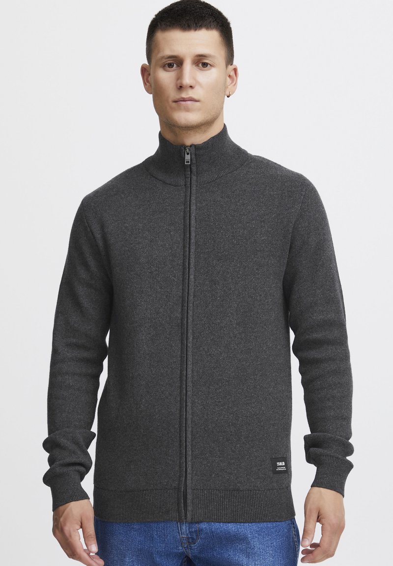 Maglione grigio con zip e colletto alto, polsini e vita a coste. Il tessuto appare morbido con una texture liscia. Etichetta del logo vicino all'orlo.