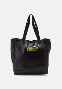 Sac fourre-tout noir texturé avec deux poignées, arborant un logo Puma doré et un emblème de chat sautant au centre à l'avant.