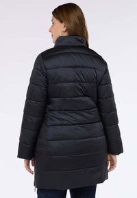 Svart vadderad jacka med hög krage, försedd med horisontella quiltade sektioner och dragkedjeförsedda sidofickor, sedd bakifrån.