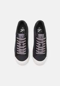 Mustat kangaskengät harmailla nauhoilla, pyöreällä kärjellä, teksturoidulla valkoisella kumipohjalla ja logotunneilla.