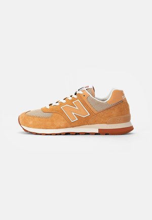 Trampki New Balance z zamszu w kolorze jasno-brązowym i beżowym oraz siateczki, z białymi sznurowadłami i gumową podeszwą, widoczne z lewej strony na białym tle.