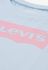 Lys blå bomulls-T-skjorte med en fremtredende rosa Levi's-logo i en buet design, med rund hals og glatt tekstur.
