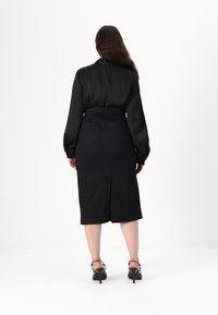 Svart satengbluse med lange ermer, kombinert med en svart denim blyantskjørt. Skjørtet har en splitt bak og to baklommer.