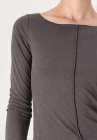 T-shirt à manches longues en matériau côtelé gris foncé avec un décolleté carré et une couture proéminente courant verticalement au centre.